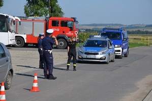 Policjantka kieruje ruchem podczas ćwiczeń, w tle  wóz strażacki i radiowozy