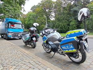 Dwa motocykle stojące na poboczu, jeden policyjny drugi  Inspektoratu Transportu Drogowego. Za motocyklami tir.
