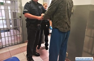 Policjant zakłada kajdanki zatrzymanemu.
