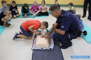 Policjant pokazuje dzieciom na manekinie jak udzielać pierwszej pomocy