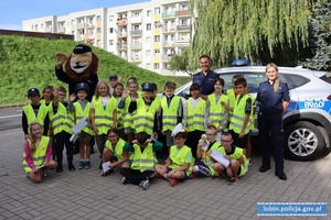 Dzieci w kamizelkach odblaskowych z na wspólnym zdjęciu z policjantką i policjantem oraz maskotką policyjną Komisarzem Lwem.