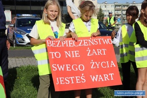 Dzieci w kamizelkach odblaskowych z plakatami z napisami: bezpieczeństwo to nie żart, swego życia jesteś wart