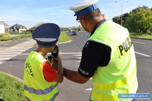 Policjant ruchu drogowego pokazuje młodemu chłopakowi, jak mierzy się prędkość radarem.