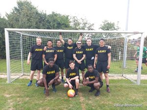 Dziesięciu mężczyzn w strojach sportowych (z amii amerykańskiej), stojących pod siatką na boisku piłkarskim i pozujący do zdjęcia drużynowego.