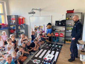 Policjant w klasie rozmawia z dziećmi siedzącymi na podłodze