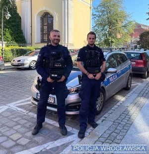 Dwóch policjantów stojących przy radiowozie