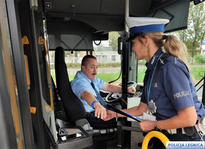 Policjantka zakłada odblaskową opaskę kierowcy autobusu siedzącemu za kierownicą.