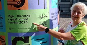 Kobieta w stroju sportowym wskazuje plakat Mistrzostw Świata w Biegach Ulicznych w Rydze