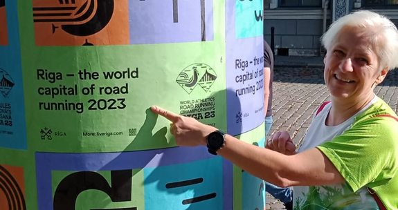 Kobieta w stroju sportowym wskazuje plakat Mistrzostw Świata w Biegach Ulicznych w Rydze