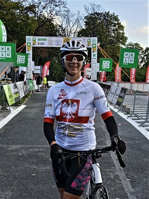 Kobieta będąca w stroju sportowym stoi na mecie trzymając rękoma rower.