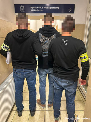 Nieumundurowani policjanci z opaskami POLICJA na ramionach prowadzą zatrzymanego mężczyznę