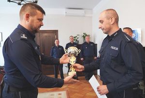 Zastępca Komendanta Wojewódzkiego Policji inspektor Norbert Kurenda przekazuje puchar policjantowi, w tle towarzyszący zwycięzcom policjanci.