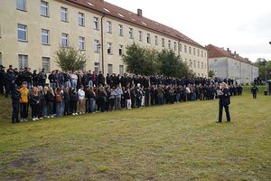 Grupa osób stojących w rzędzie na wzniesieniu przed murawą