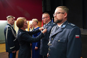 Przedstawicielka Wojewody dolnośląskiego przypina medal policjantowi. W tle pozostali odznaczeni policjanci. Asystuje jej Komendant Wojewódzki Policji we Wrocławiu.