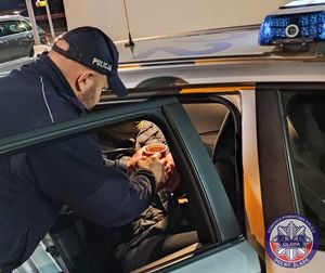 Policjant podaje bezdomnemu siedzącemu w radiowozie ciepłą herbatę.