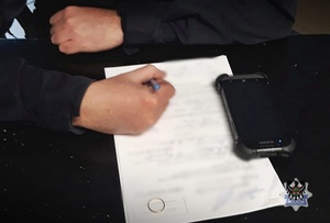 Mężczyzna podpisujący zapisaną kartkę, obok leży telefon i pierścionek.
