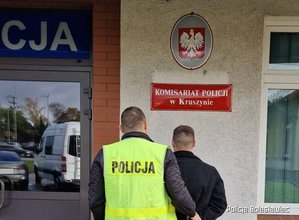 Policjant prowadzi zatrzymanego mężczyznę do budynku komisariatu policji w Kruszynie