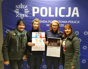 Policjantki z kalendarzami na tle banneru Komenda Powiatowa Policji w Jaworze