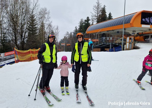Na stoku. Dwaj policjanci na nartach trzymają dziewczynę na nartach za ręce.