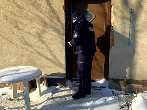 Policjant stoi przy drzwiach domu.