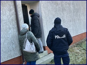 Policjant i dwie osoby w cywilu stoją przed drzwiami banku