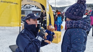Policjant mówiący przez mikrofon przekazuje dziewczynce maskotkę Komisarza Lwa