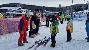 Instruktor narciarstwa pokazuje dzieciom jak właściwie zakładać narty obok Komisarz Lew