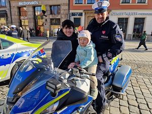Dziecko siedzące na policyjnym motorze, z tyłu policjant i obok kobieta.