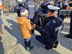 Dziecko uderzą w bęben, który trzyma policjant z orkiestry policyjnej