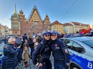 Dwie policjantki stojące koło radiowozu z tyłu tłum ludzi podczas festiwalu  Wielkiej Orkiestry Świątecznej Pomocy.