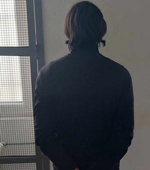 Na zdjęciu widoczny mężczyzna, który stoi twarzą do ściany, czyli tyłem do osoby wykonujących zdjęcie. Mężczyzna ubrany w ciemną bluzę, włosy długie, koloru ciemnego.