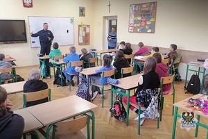 Policjant mówi do dzieci siedzących w ławkach w szkolnej klasie