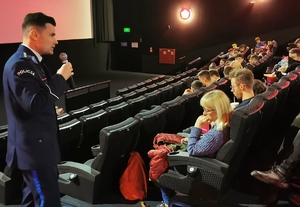 Policjant przemawia do młodzieży siedzącej w sali kinowej