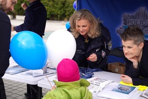 Dziecko z balonami stojące przy stoisku profilaktycznym, gdzie są uśmiechnięte policjantki