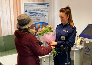 Starsza kobieta wręcza kwiaty policjantce