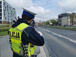 Policjant ruchu drogowego dokonujący na ulicy pomiaru prędkości ręcznym miernikiem prędkości