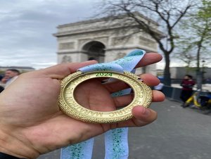 Mężczyzna trzyma w ręce medal na tle łuku triumfalnego w Paryżu