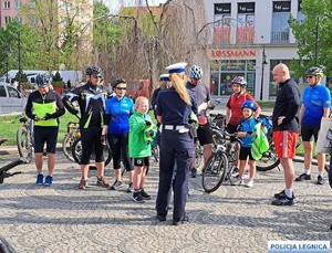 Umundurowany policjant i policjantki w trakcie spotkania profilaktycznego z uczestnikami wycieczki rowerowej.