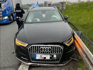 Audi które uderzyło w boczne barierki na drodze A4 - zdjęcie z przodu auta, obok samochodu policjantka