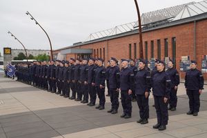 Nowo przyjęci policjanci stojący w dwuszeregu podczas śpiewania hymnu
