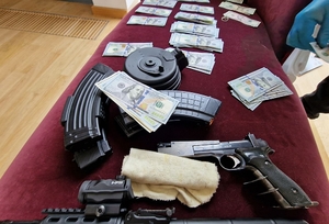 Przedmioty znalezione w przeszukiwanych mieszkaniach - rozłożone na stole banknoty po 100 dolarów i broń