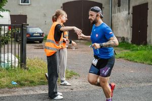 POLICJANT BIEGNIE W MARATONIE, DZIEWCZYNA Z OBSŁUGI TECHNICZNEJ PODAJE MU WODĘ DO PICIA W KUBECZKU