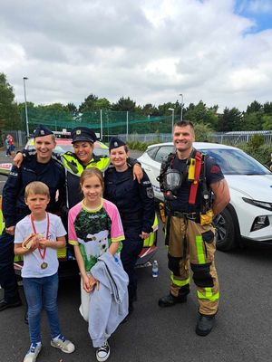 Policjantki z Polski z policjantką z Irlandii oraz strażakiem wraz z dwójką dziećmi stoją przed radiowozem