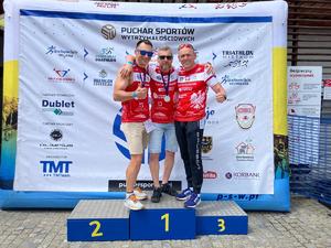 trzech mężczyzn z medalami stoją na podium