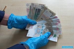 Ręce w rękawiczkach trzymają banknoty w polskim nominale rozłożone w wachlarz