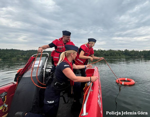 policjanci na łodzi ratunkowej rzucają koło ratunkowe