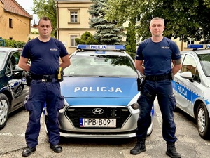 Dwóch policjantów stojących przed radiowozem