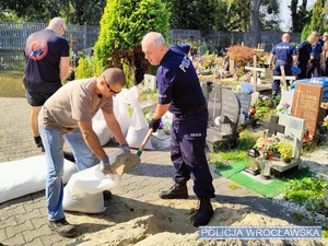 Policjanci układają worki na cmentarzu