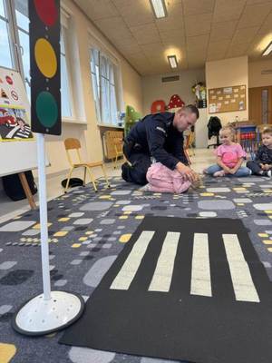 policjant w przedszkolu pokazuje dziecku pozycję obronną na żółwia