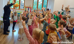 Policjantka w klasie podnosi ręce do góry razem z dziećmi